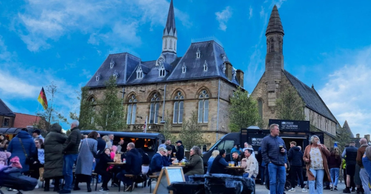 group of people sitting, eating and drinking with food trucks in background at Bishop Auckland Market Place